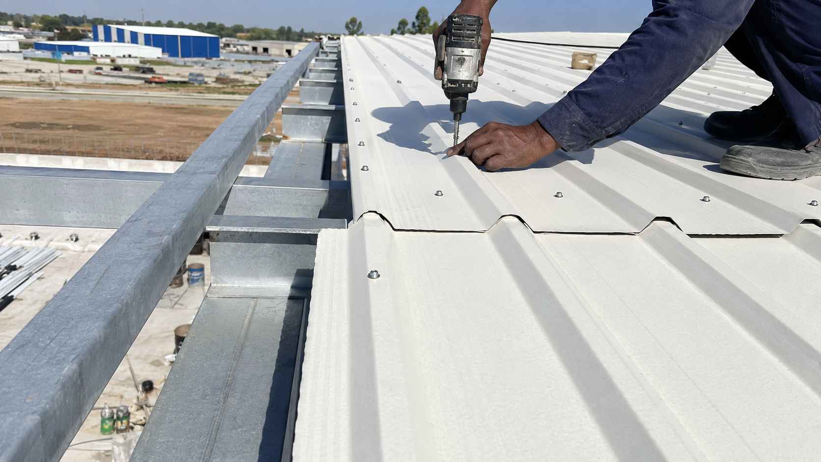 Pure-white galvalume profiled steel sheeting being fixed to the purlins of a PEB steel structure.