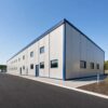 Long side elevation of a grey PEB steel structure with navy roofline trim on a paved site.