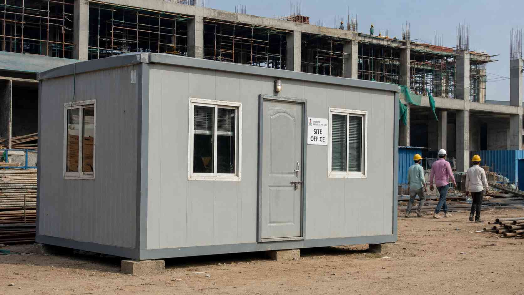 Pearl grey porta cabin functioning as a contractor's site office on an Indian construction project, daylight.