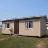 Sandstone beige porta cabin house on an open residential plot, set up as a home.