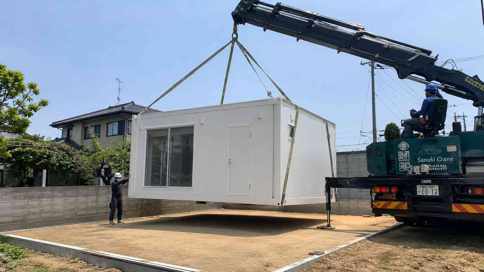 White portable cabin house lifted by a crane onto a residential base, delivered whole