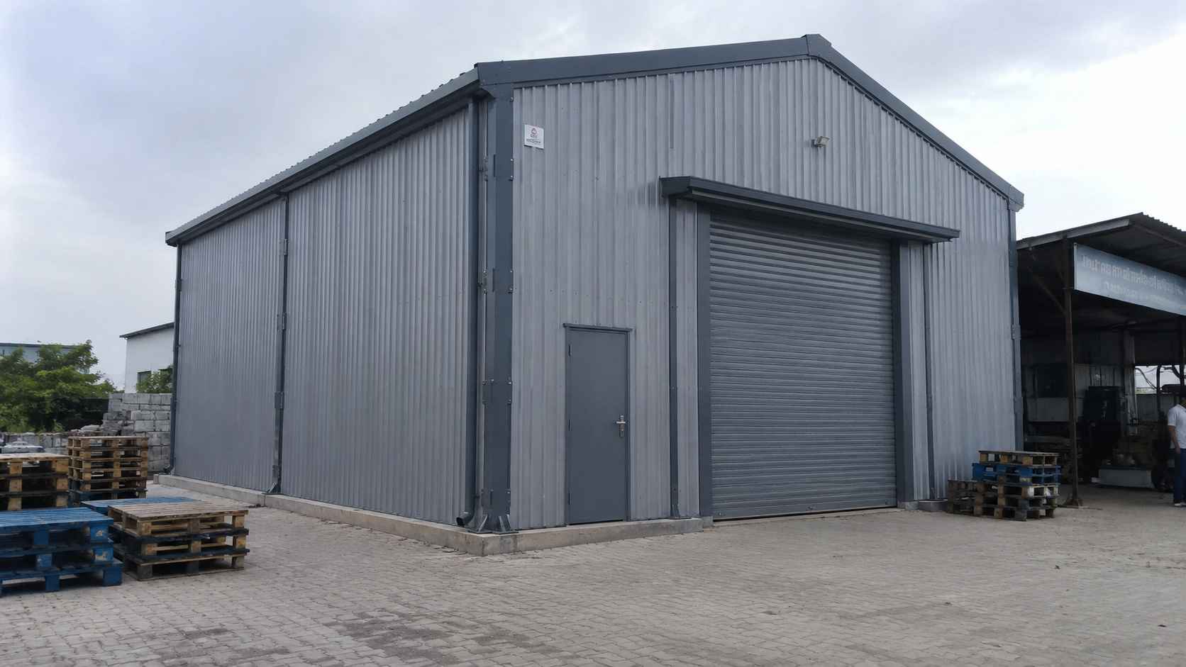 Steel-grey 40×30 ft portable shed on an Indian industrial yard with a roller door