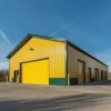Yellow pre-engineered building with green trim and several roller-shutter bays on a paved commercial apron.