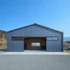 Grey pre-engineered building structure with an open central bay showing the column-free clear-span interior.