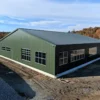 Green and black pre-engineered building structure on a gravel industrial site, side and length view.
