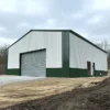 White and green pre-engineered building structure on an active site with roller shutter, near completion.