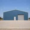 Front gable elevation of a steel-blue pre-engineered building showing door and roller shutter