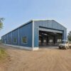 Steel-blue pre-engineered building with open roller shutter showing column-free interior access