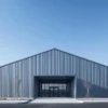 Grey pre-engineered steel building with a glass front entrance and gable roof on a paved industrial plot.
