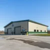 Grey and beige pre-engineered steel building with two black roller shutters on a paved factory apron.
