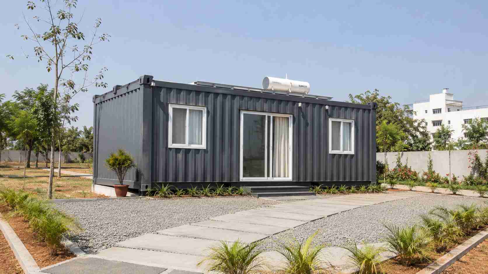 Charcoal prebuilt container home seen whole from the plot approach, delivered as one unit.