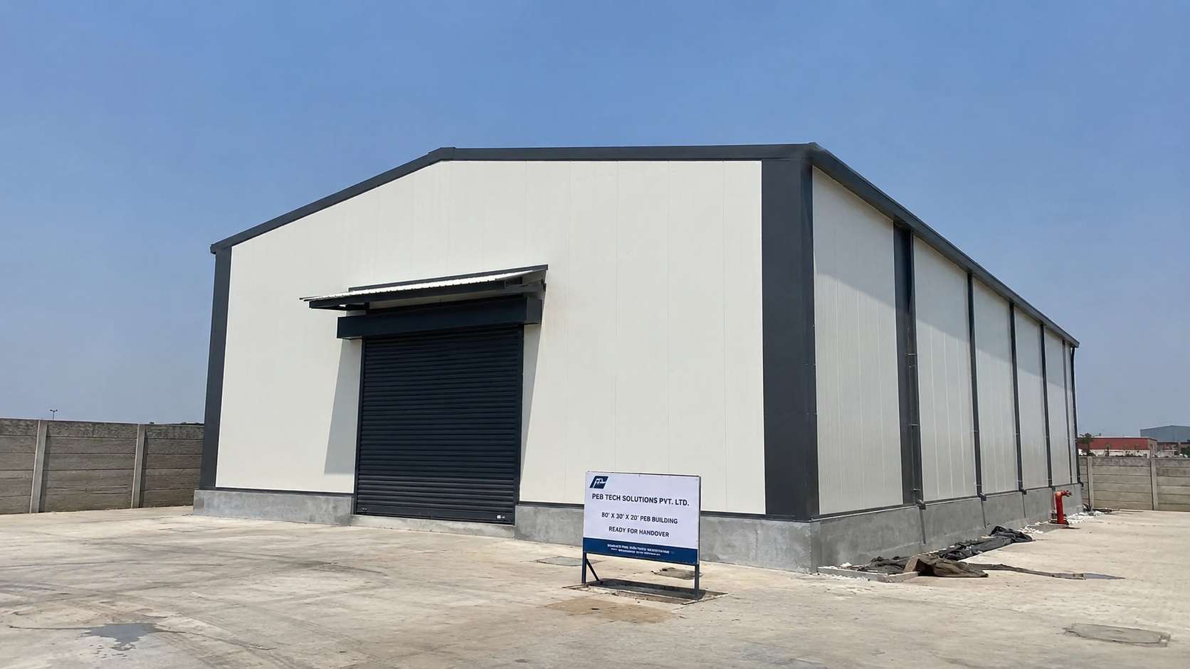 White PUF-panel prefab building, 80 by 30 ft, with charcoal trim ready for handover on a concrete apron.