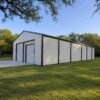 White prefab steel building with charcoal trim standing complete on a cleared plot.