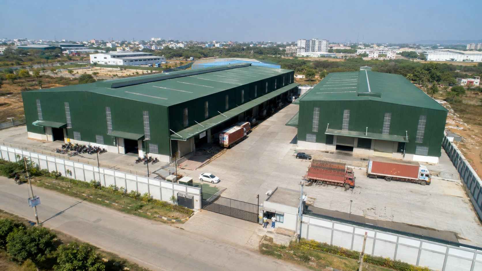 Aerial of a green multi-bay prefab building complex with internal road on an Indian industrial zone.