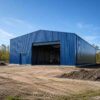 Blue prefab building under construction on a prepared site, front entry open before cladding completion.