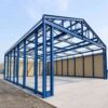 Blue structural steel frame of a prefab building before cladding, showing portal frames and rafters.