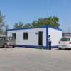 White prefab building in use as an office at an Indian industrial compound with parked vehicles.