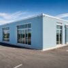 Steel-blue prefab commercial building with large glazed display windows facing a customer car park.