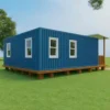 Side elevation of SAMAN marine blue prefab container home raised on wooden plinth with three white-trimmed openable windows.