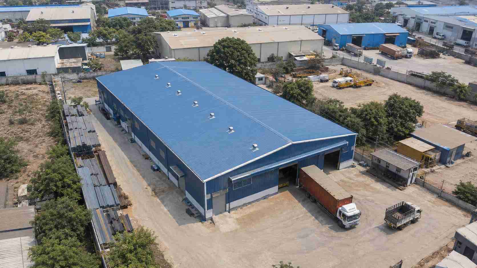 Aerial view of a steel-blue prefab manufacturing building among factory and warehouse units.