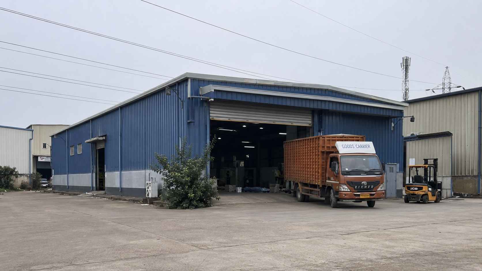 Steel-blue prefab manufacturing building in an Indian industrial estate with a forklift at the entry.
