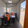 Engineers in Safety Orange PPE reviewing drawings inside a SAMAN cabin-form mobile workspace interior.