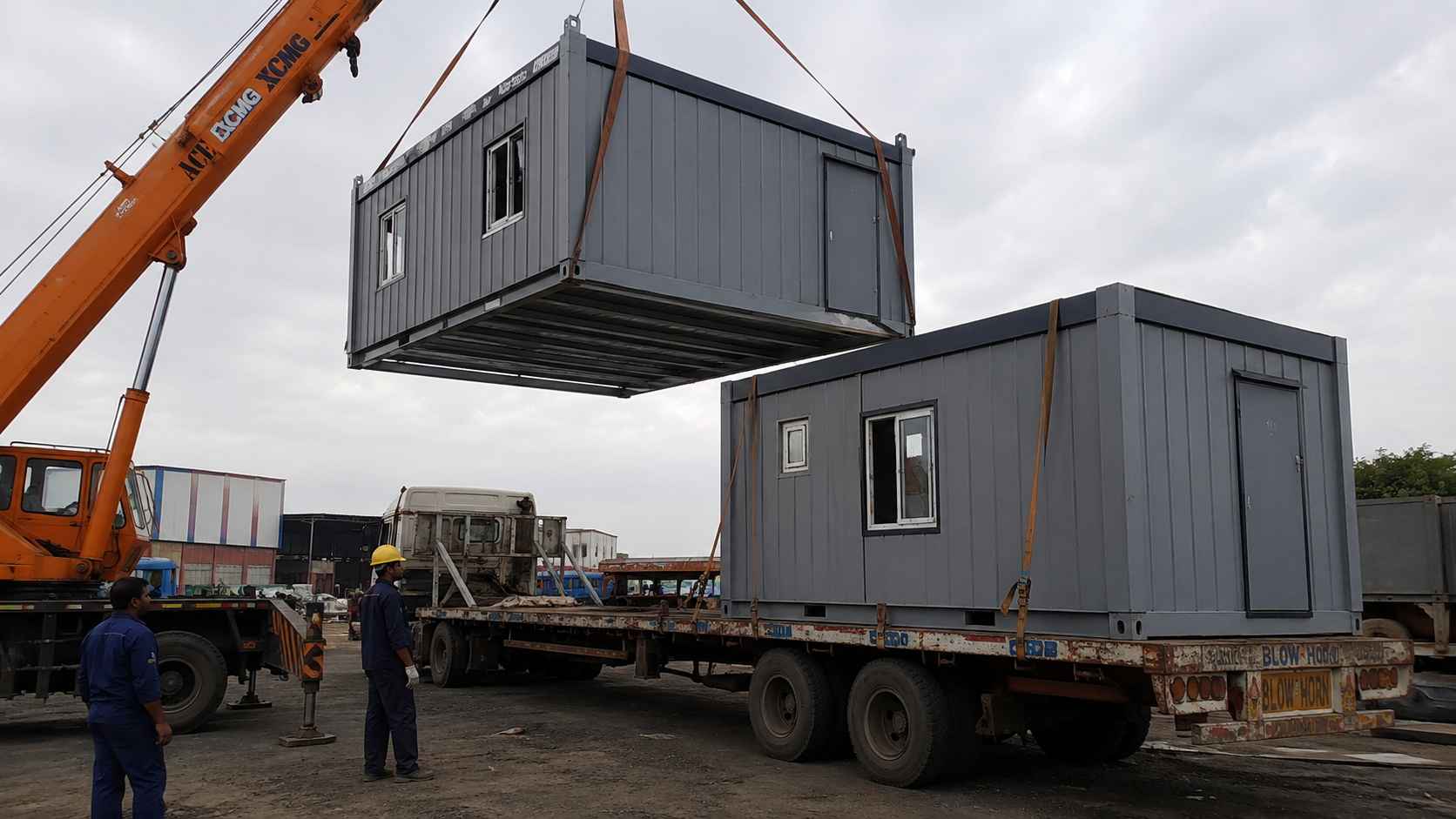 Steel-grey modular building section craned onto a flatbed trailer for relocation to a new site.