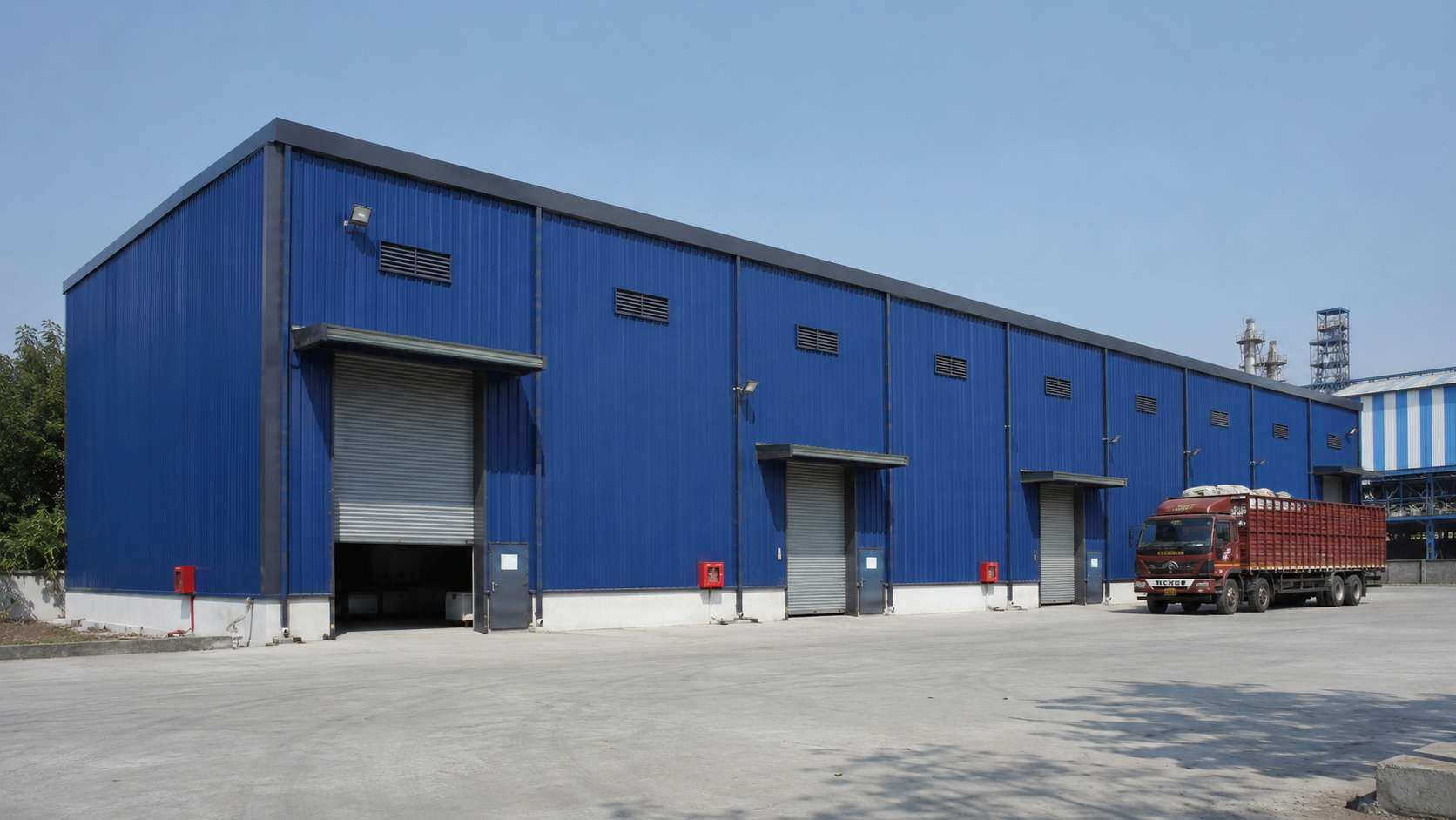 Royal-blue multi-bay prefab modular building extended in stages across an industrial zone.