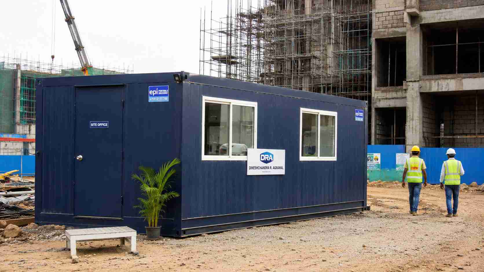 Navy blue prefab site office on an active construction site with workers nearby.