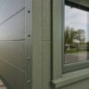 Close-up of a sage green steel house wall panel meeting a sealed window frame.