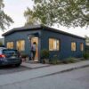 teel blue prefab steel house in use, person at the door with a car and plants outside.
