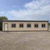 Sandstone beige prefab steel house side view showing a window line and a personnel door.