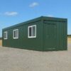 A forest green prefabricated bunkhouse unit on a level base, three-quarter front view in clear daylight.