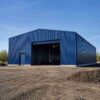 Front gable of a blue prefabricated steel building with an open bay, on an industrial site.