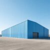 Large blue prefabricated steel building completed and standing on an industrial plot.