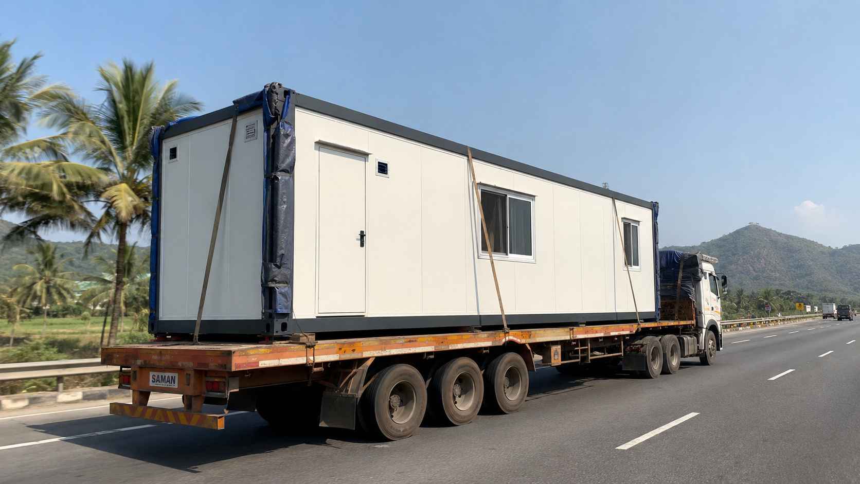 Pure white prefabricated container house on a hydraulic flatbed trailer travelling on an Indian highway