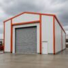 Pale yellow prefabricated industrial shed with black gable roof and hinged double doors.