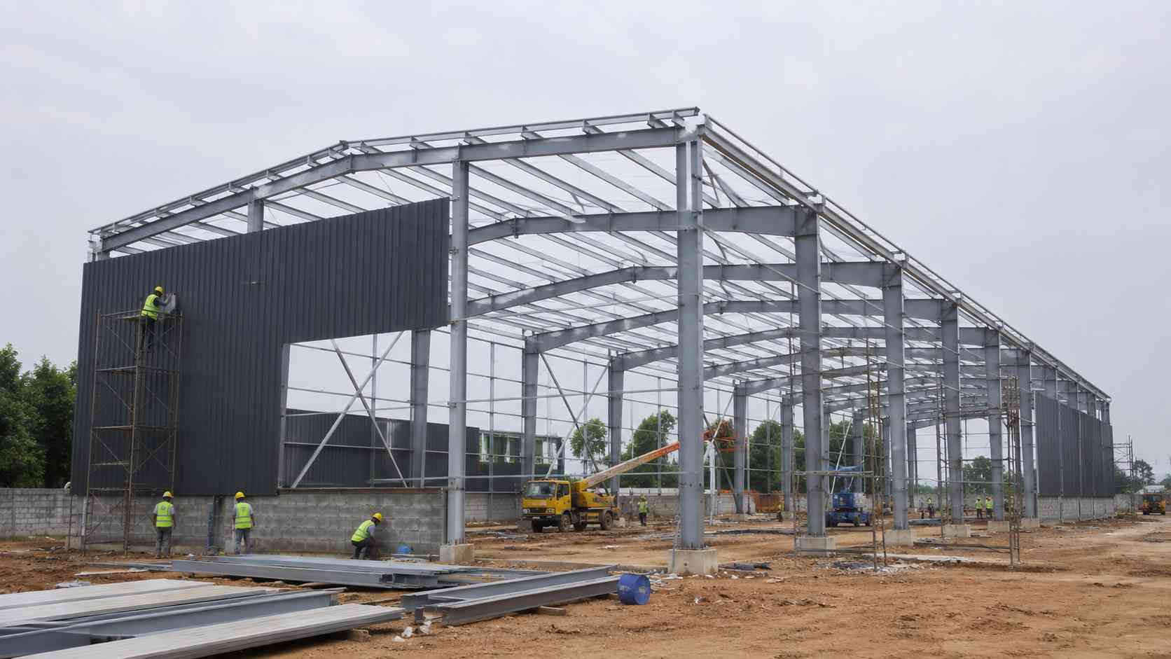 Erected clear-span structural steel frame of a prefabricated steel building with partial charcoal cladding.