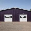 Front gable of a prefabricated steel building in deep purple with two white sectional doors.