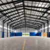 Interior steel frame of a prefabricated steel building showing grey columns, rafters and a clear-span roof.