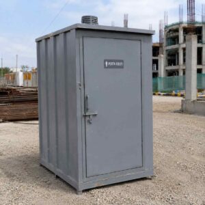 Steel grey readymade toilet cabin on a gravel pad at a construction site.
