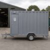 Side view of a steel grey readymade toilet cabin showing depth and roof vent.