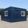 Navy blue 20×20 ft SAMAN prefab office cabin on a level concrete pad, front three-quarter view.