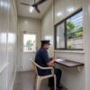 Interior of a SAMAN security guard cabin with a guard at the register counter under a ceiling fan