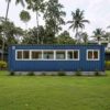 Side view of a steel-blue 40-ft shipping container home with white-framed windows on a plot