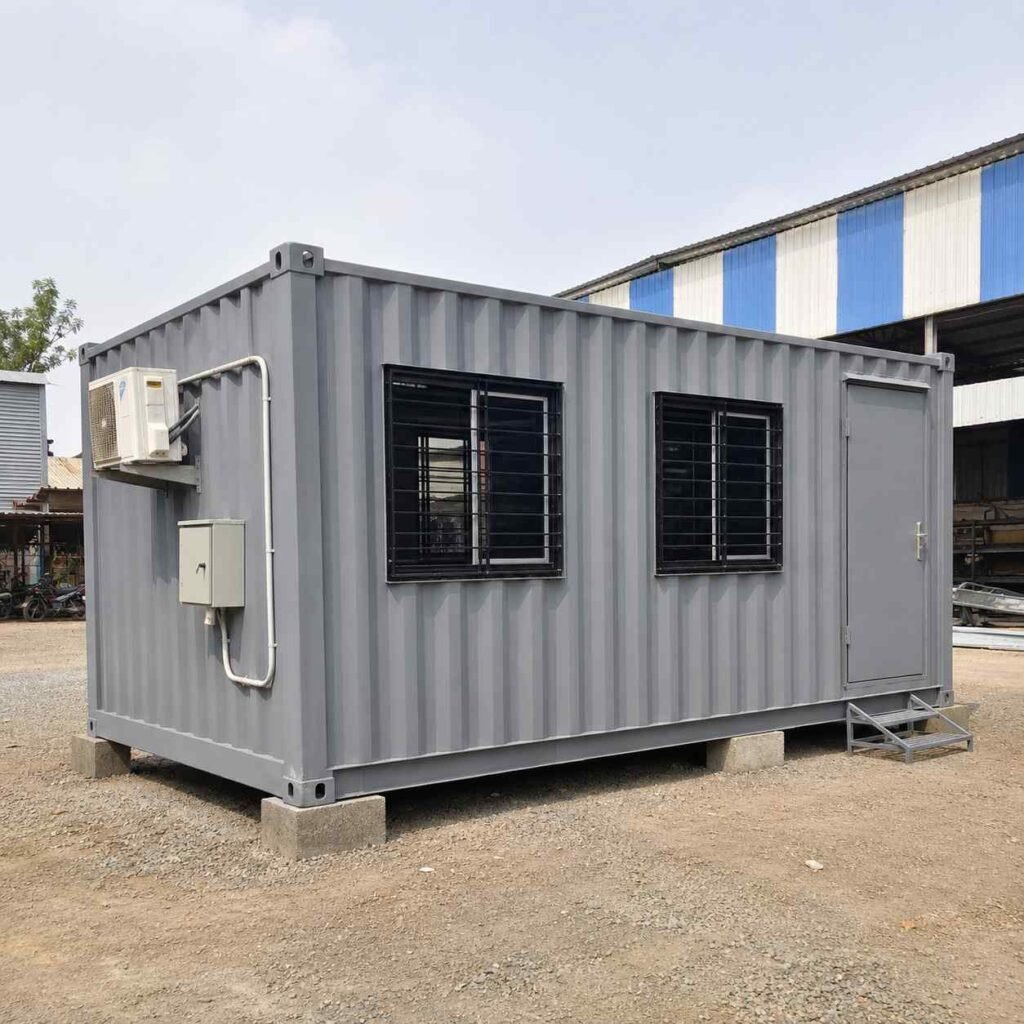 Steel grey 20-ft shipping container office in three-quarter front view at an Indian project site.