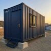 Navy blue 20-ft shipping container office front-angle view showing steel door, access step, and concrete foundation.