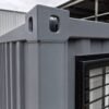 Macro detail of a steel grey shipping container office ISO corner casting and corrugated panel weld line.