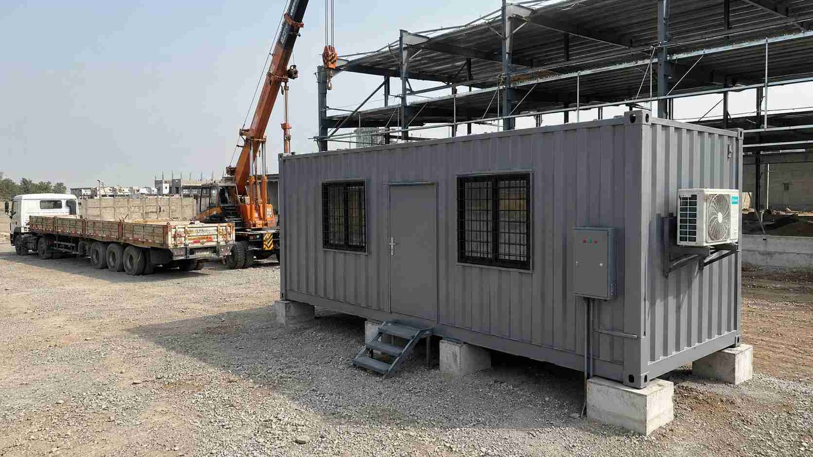 Steel grey shipping container office freshly delivered to an Indian warehouse construction site with delivery truck visible.