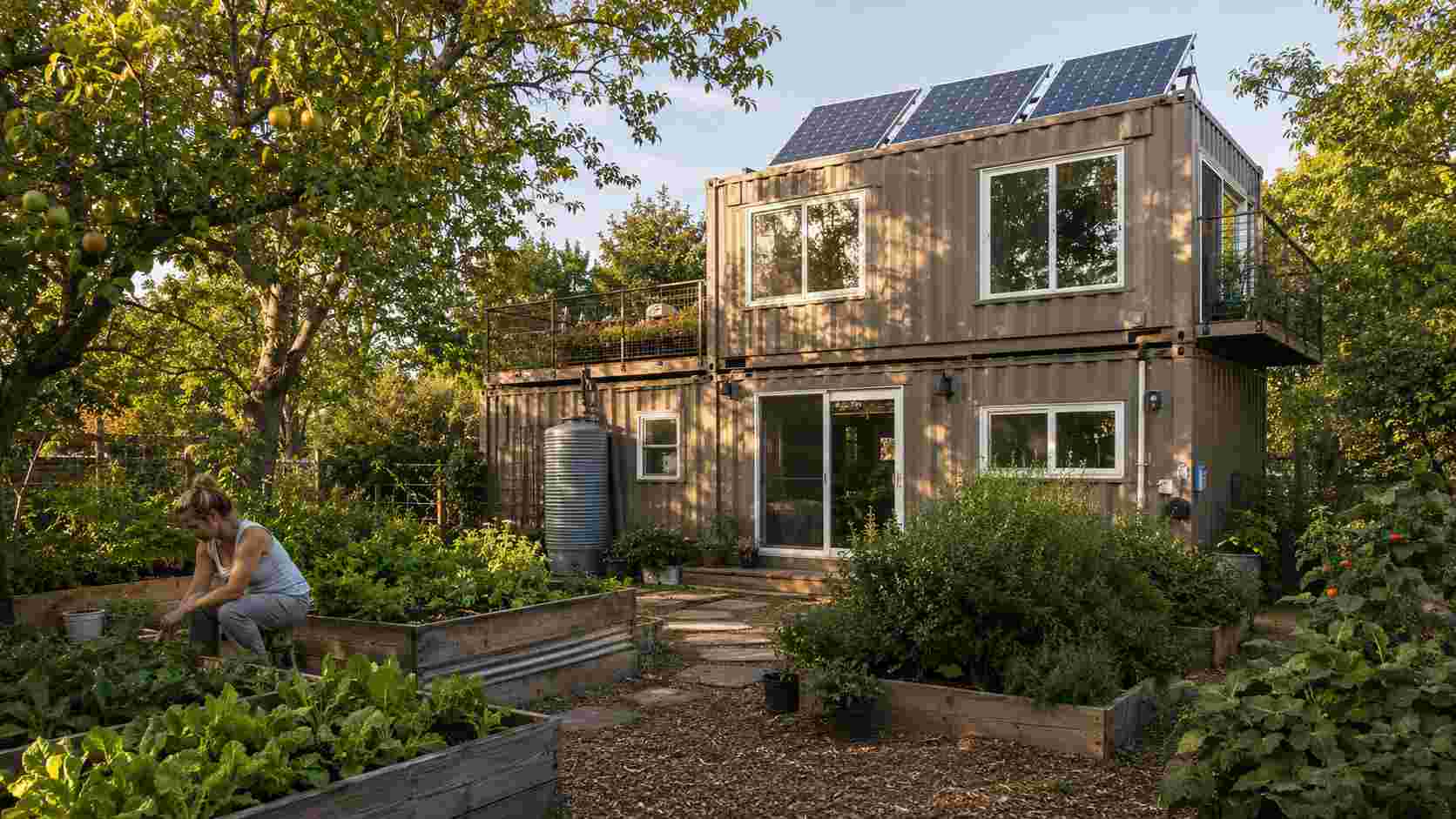 shipping container tiny house in eco garden setting with solar panels warm taupe exterior and vegetable planters
